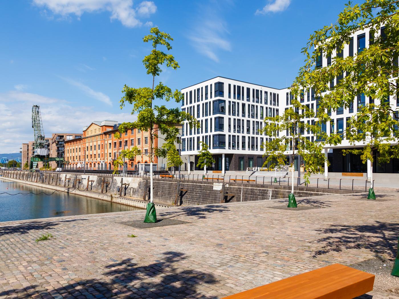 Der Zollhafen in Mainz: das Hafenbecken mit dem alten Hafenkran, dahinter neue Wohn- und Bürohäuser, davor die gepflasterte Promenade