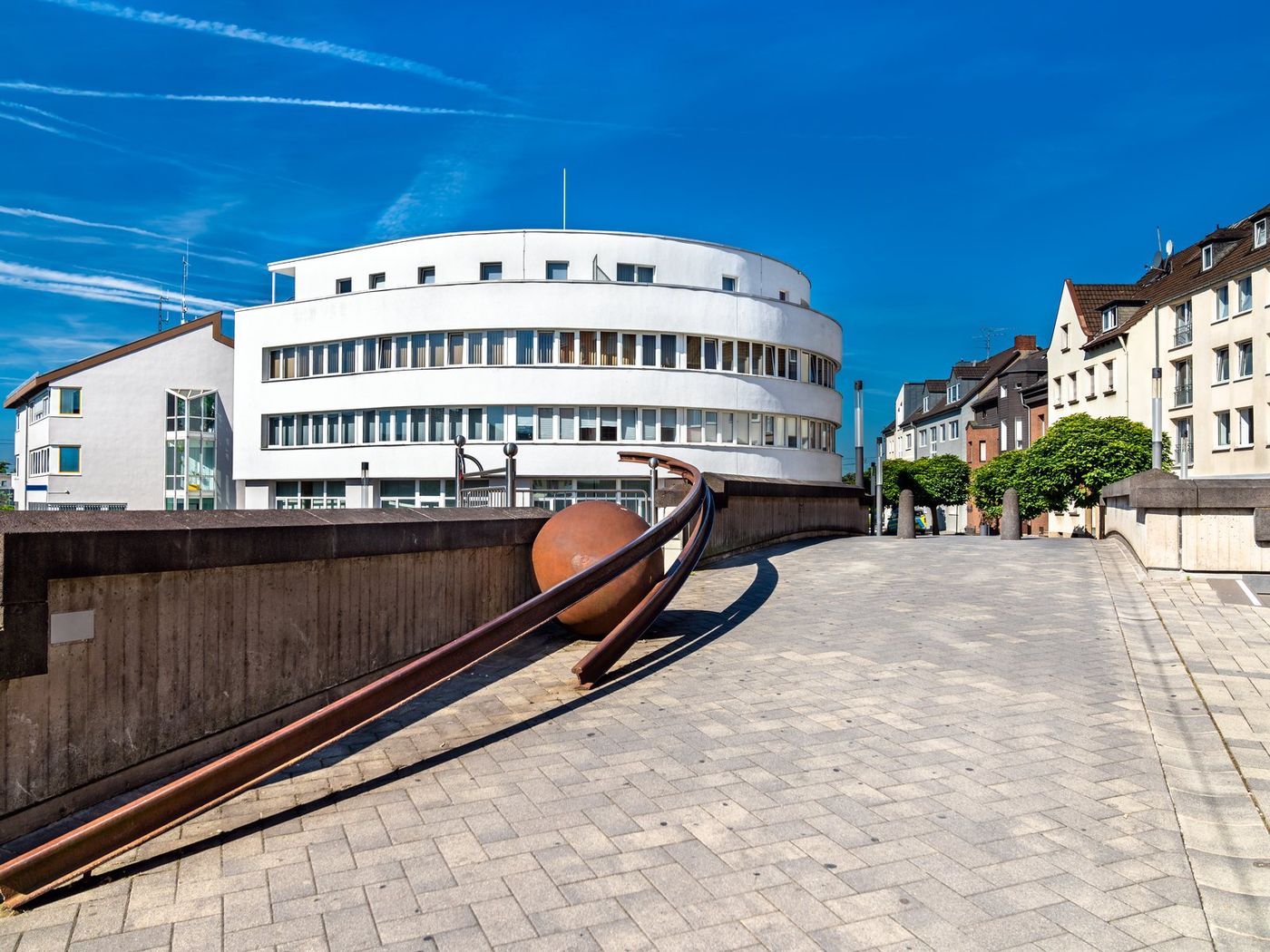 Innenstadt von Troisdorf: gepflasterter Platz mit rostroter Stahlskulptur vor einem runden weißen Gebäude